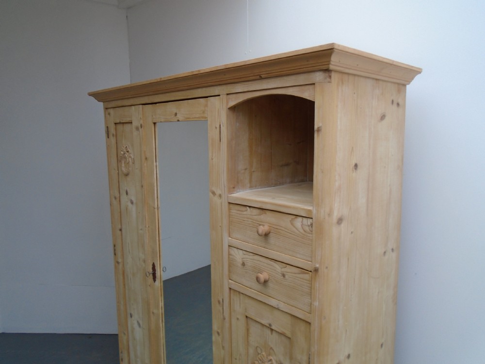 A large Victorian stripped pine wardrobe featuring a central mirrored door, carved ribbon relief motifs, an open alcove, drawers, and turned bun feet. View II