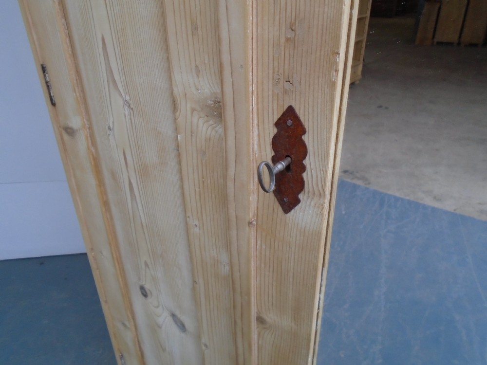 A large Victorian stripped pine wardrobe featuring a central mirrored door, carved ribbon relief motifs, an open alcove, drawers, and turned bun feet. View VIII