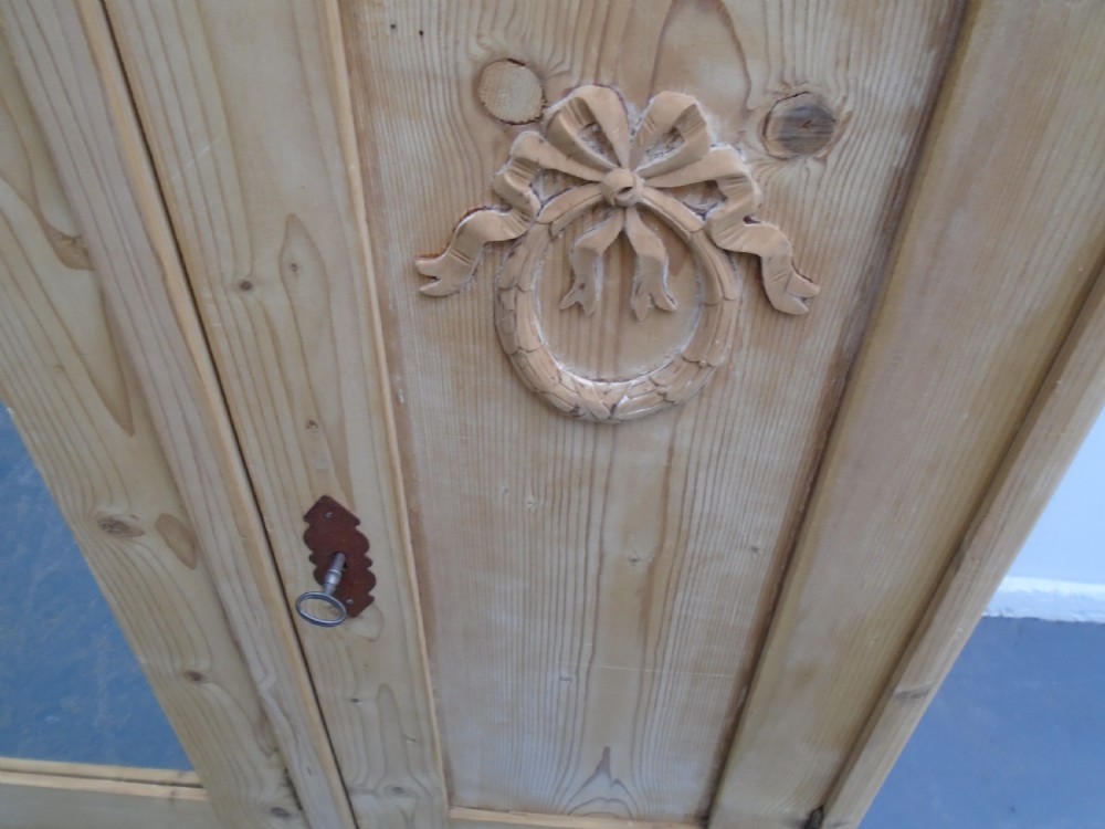 A large Victorian stripped pine wardrobe featuring a central mirrored door, carved ribbon relief motifs, an open alcove, drawers, and turned bun feet. View IX