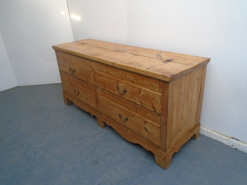 An extra wide Georgian waxed pine blanket box featuring a hinged top lid, brass swan-neck handles, faux drawer fronts, and a bracket base.