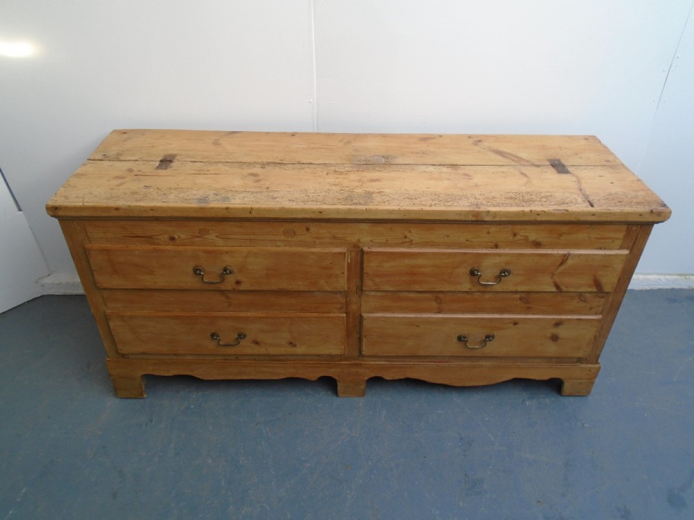 An extra wide Georgian waxed pine blanket box featuring a hinged top lid, brass swan-neck handles, faux drawer fronts, and a bracket base. View II