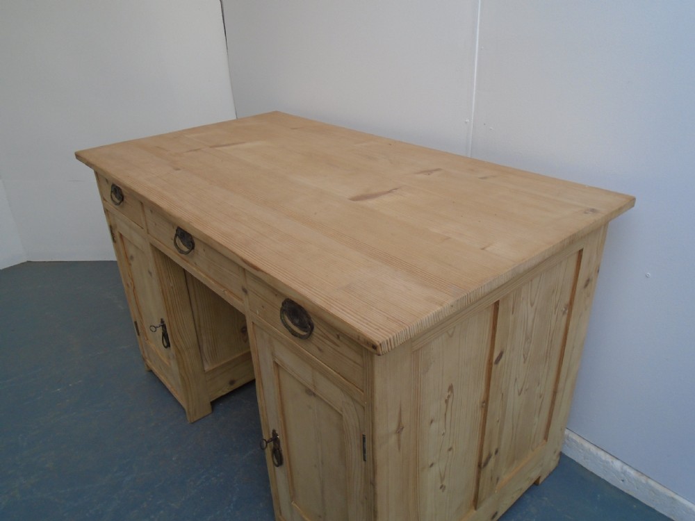 A large Victorian stripped pine pedestal desk featuring three top drawers, two panelled cupboard doors, and metal drop pull handles. View II