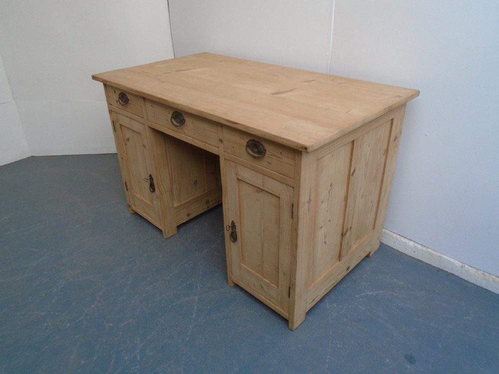 A large Victorian stripped pine pedestal desk featuring three top drawers, two panelled cupboard doors, and metal drop pull handles.