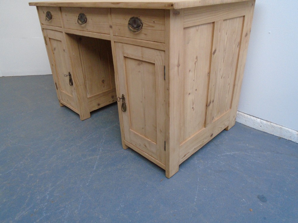 A large Victorian stripped pine pedestal desk featuring three top drawers, two panelled cupboard doors, and metal drop pull handles. View III