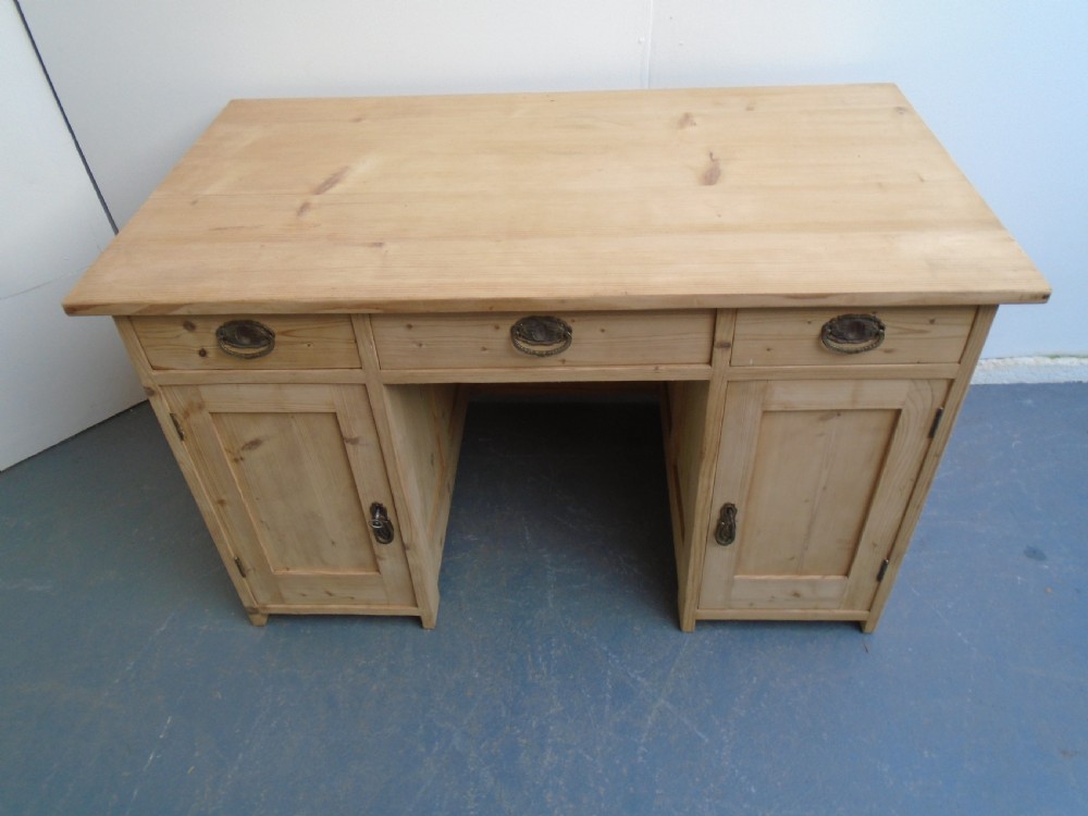 A large Victorian stripped pine pedestal desk featuring three top drawers, two panelled cupboard doors, and metal drop pull handles. View IV