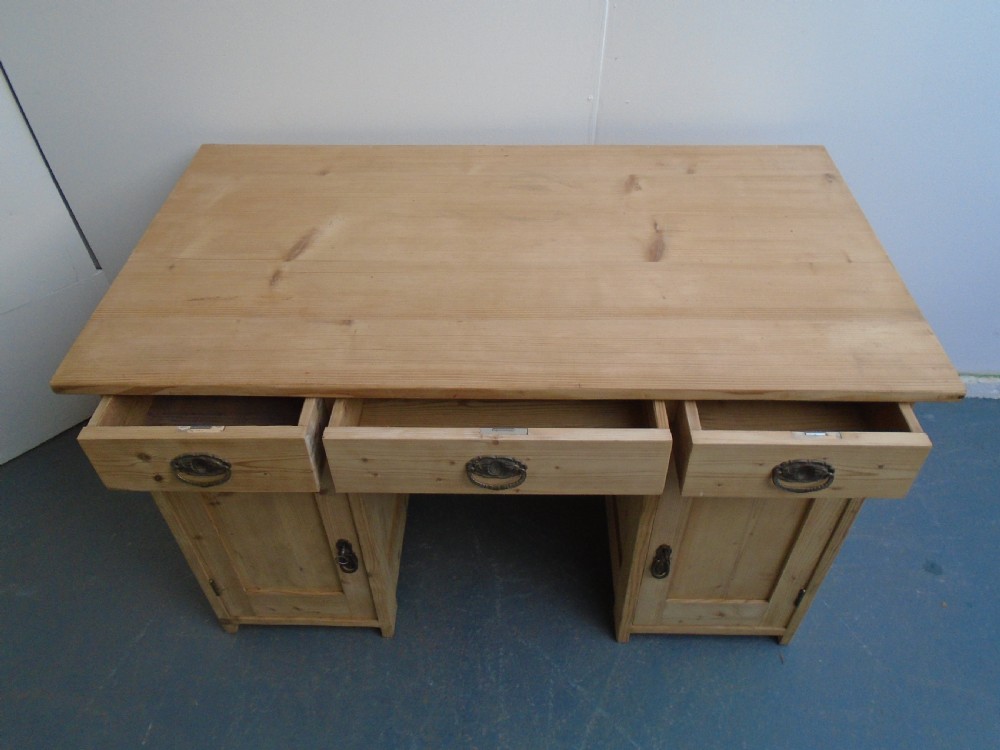 A large Victorian stripped pine pedestal desk featuring three top drawers, two panelled cupboard doors, and metal drop pull handles. View VII