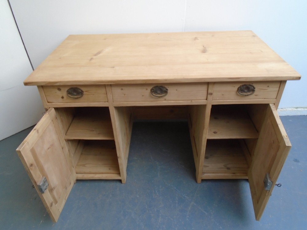 A large Victorian stripped pine pedestal desk featuring three top drawers, two panelled cupboard doors, and metal drop pull handles. View X