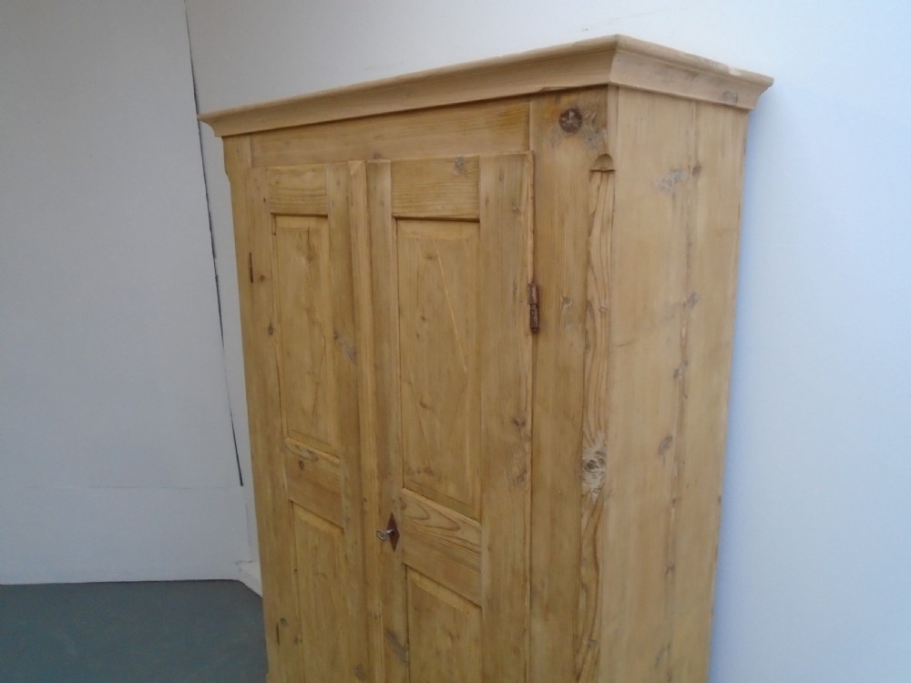 A tall Georgian natural pine storage cupboard featuring two fielded panel doors above a wide base drawer, set on turned bun feet. View II
