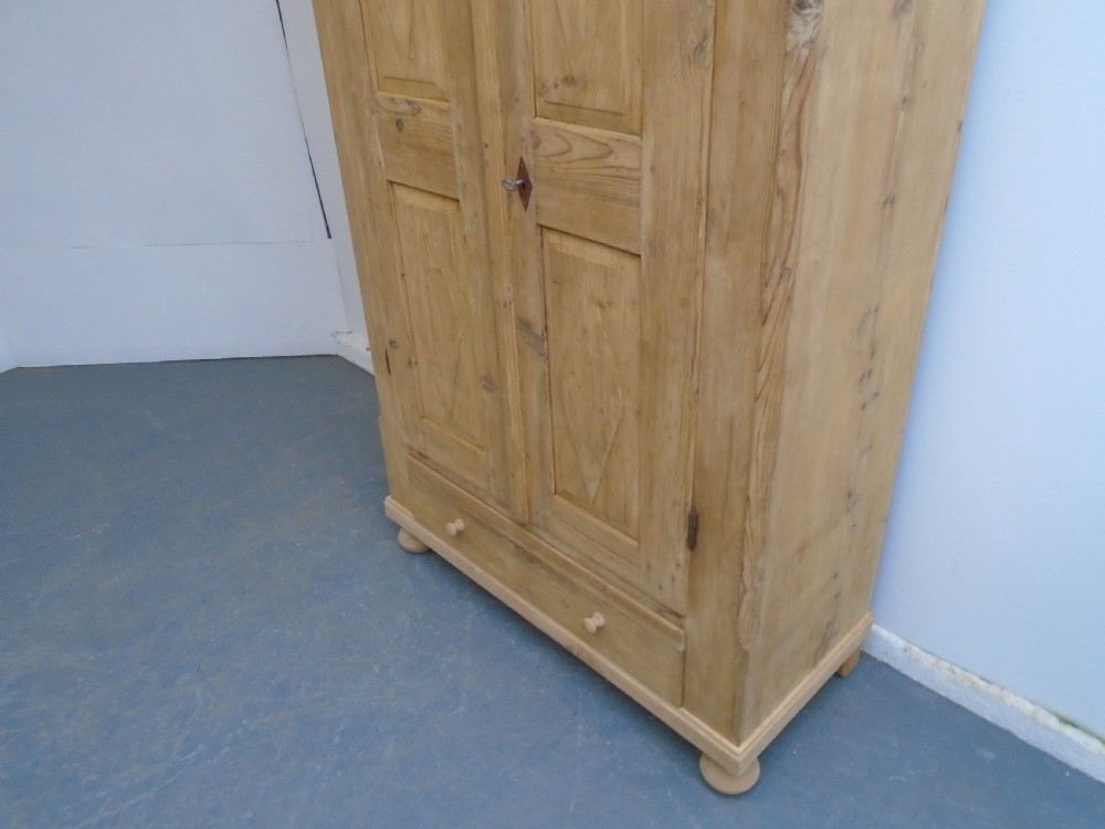 A tall Georgian natural pine storage cupboard featuring two fielded panel doors above a wide base drawer, set on turned bun feet. View III