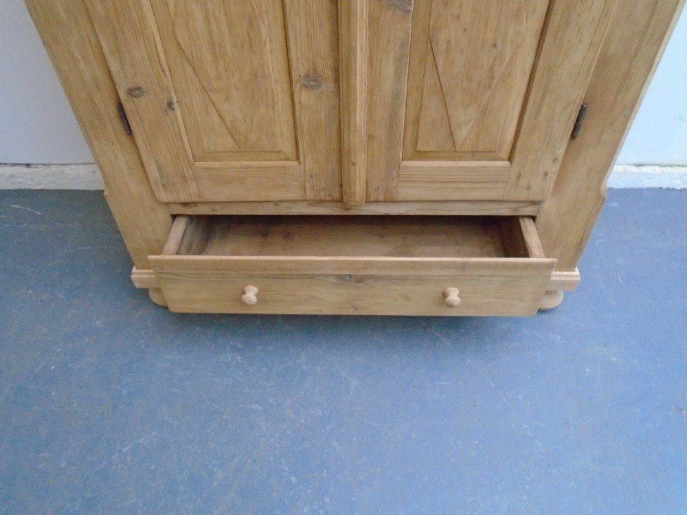 A tall Georgian natural pine storage cupboard featuring two fielded panel doors above a wide base drawer, set on turned bun feet. View IX