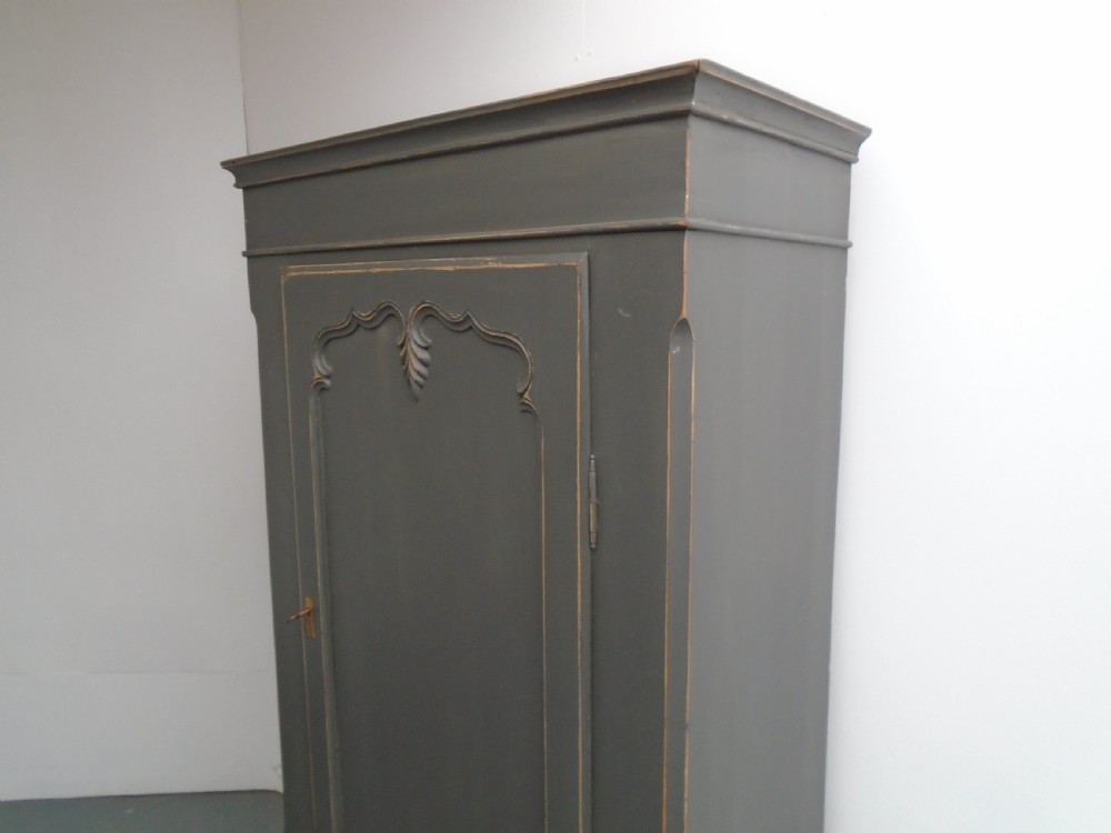 A dark grey painted pine storage cupboard featuring a single panelled door with relief carving, a bottom drawer, and a stepped cornice. View II