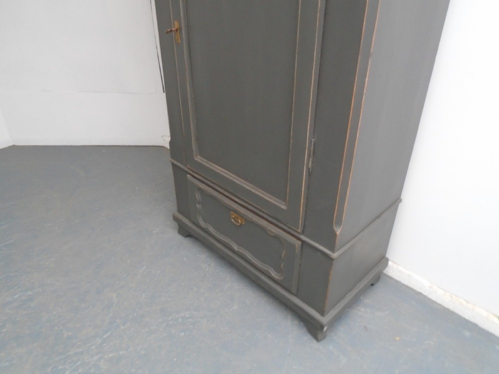 A dark grey painted pine storage cupboard featuring a single panelled door with relief carving, a bottom drawer, and a stepped cornice. View III