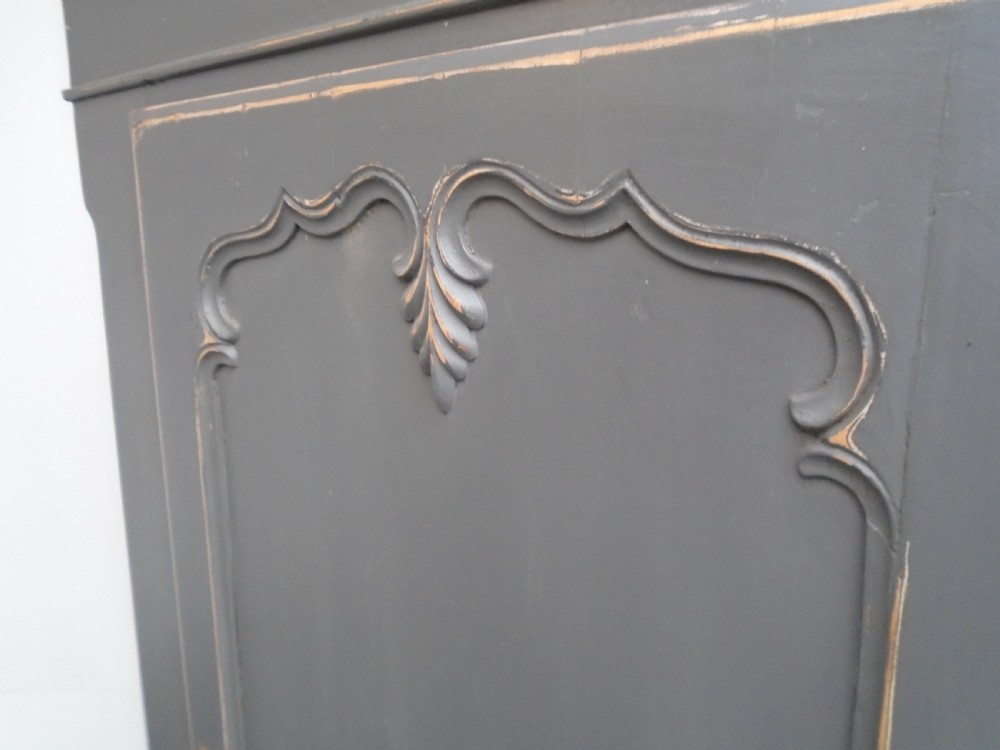 A dark grey painted pine storage cupboard featuring a single panelled door with relief carving, a bottom drawer, and a stepped cornice. View VI