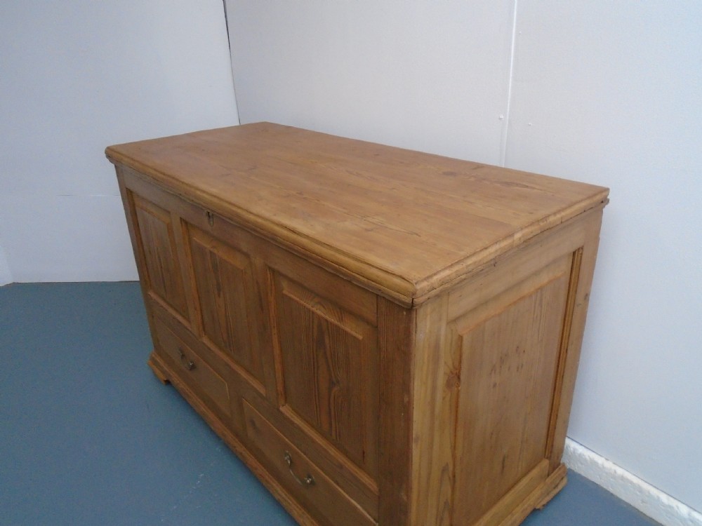 A waxed pine Georgian mule chest featuring a hinged top lid, three front panels, two lower drawers with brass handles, and a moulded plinth base. View II