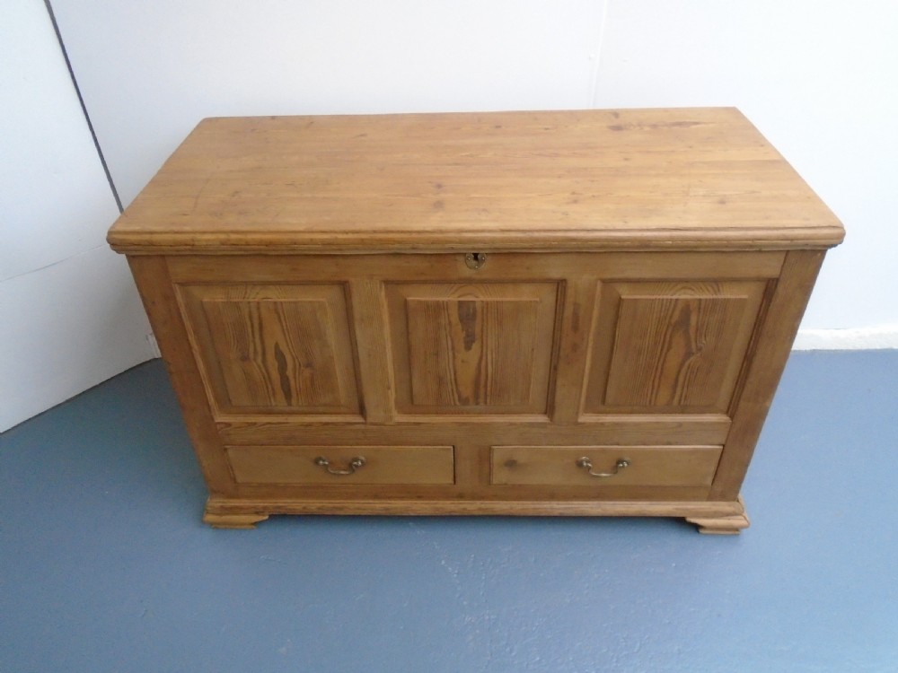 A waxed pine Georgian mule chest featuring a hinged top lid, three front panels, two lower drawers with brass handles, and a moulded plinth base. View VII