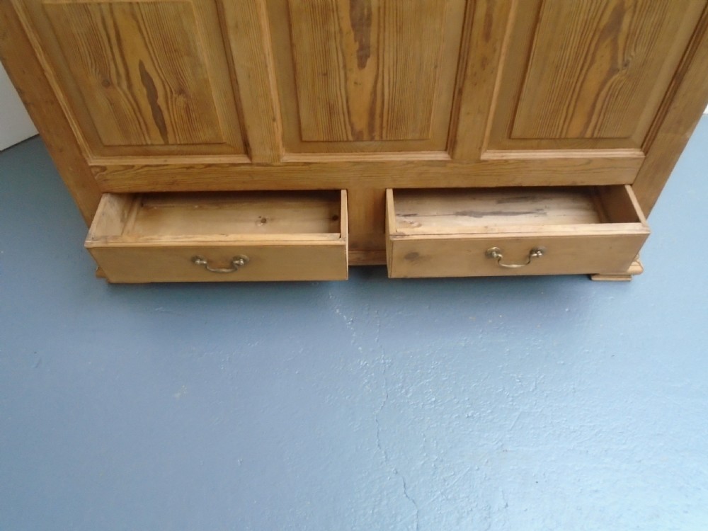 A waxed pine Georgian mule chest featuring a hinged top lid, three front panels, two lower drawers with brass handles, and a moulded plinth base. View X