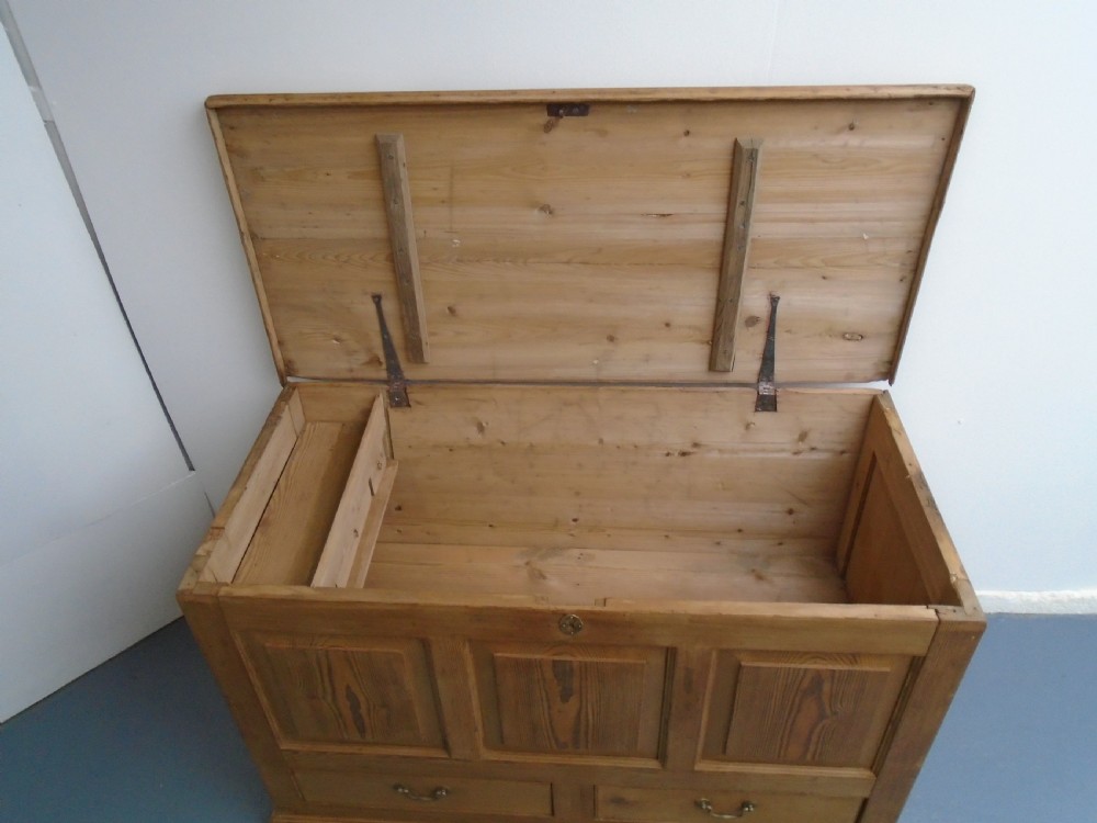 A waxed pine Georgian mule chest featuring a hinged top lid, three front panels, two lower drawers with brass handles, and a moulded plinth base. View XII