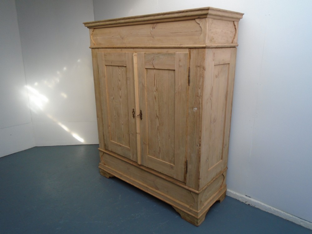An unpainted Georgian pine two-door wardrobe featuring recessed panel doors, side panel construction, and a prominent moulded upper cornice.