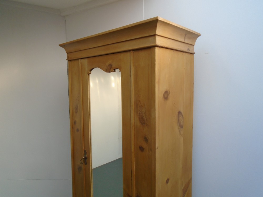 A single-door waxed pine wardrobe featuring a shaped central mirror, lower drawer with brass drop handles, and a moulded top cornice. View II