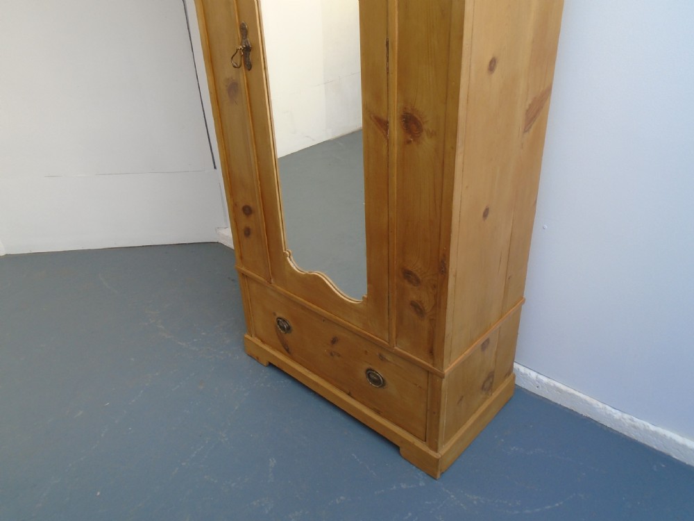 A single-door waxed pine wardrobe featuring a shaped central mirror, lower drawer with brass drop handles, and a moulded top cornice. View VII