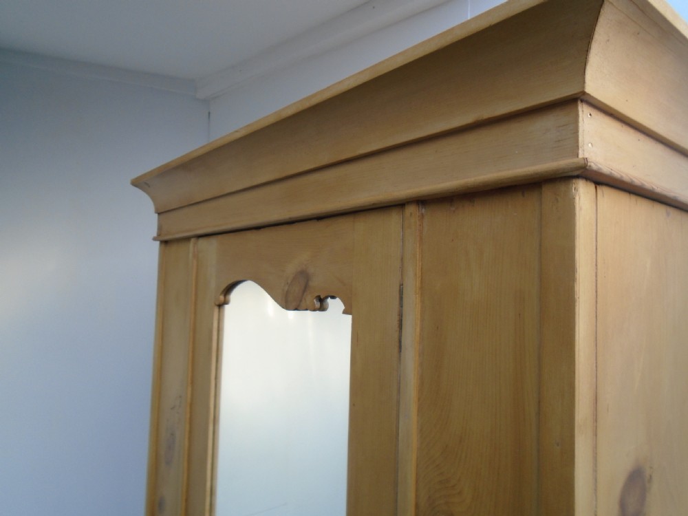 A single-door waxed pine wardrobe featuring a shaped central mirror, lower drawer with brass drop handles, and a moulded top cornice. View X