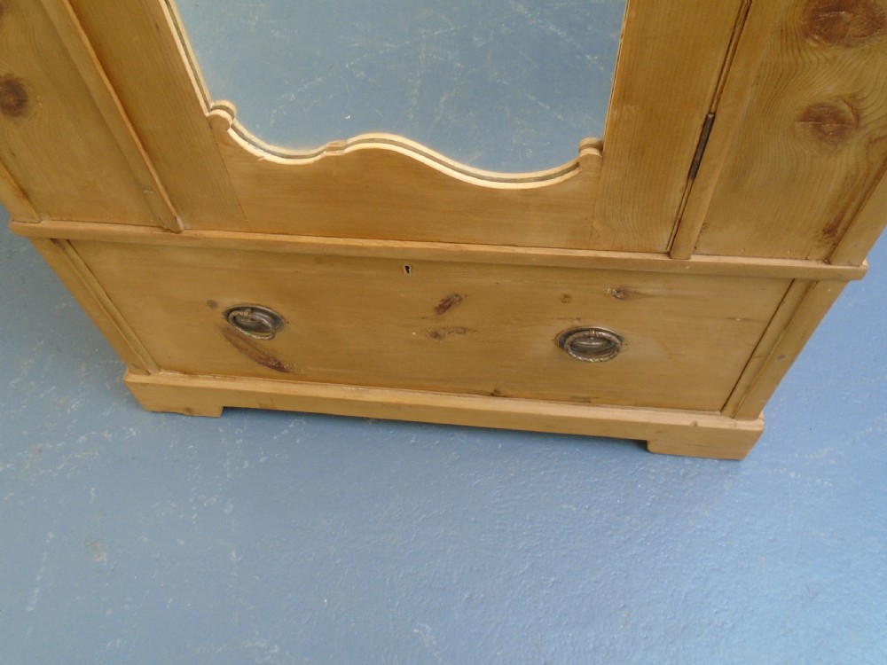 A single-door waxed pine wardrobe featuring a shaped central mirror, lower drawer with brass drop handles, and a moulded top cornice. View XII