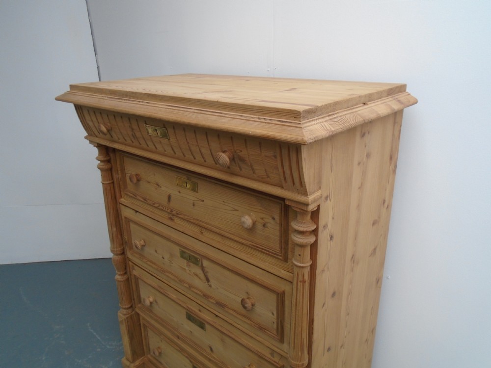 A tall Victorian stripped pine chest featuring five drawers, turned side columns, wooden knobs, and brass escutcheons. View II