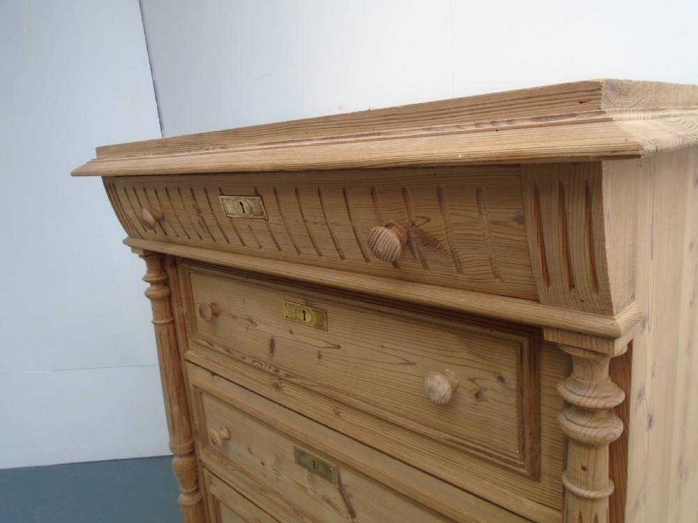 A tall Victorian stripped pine chest featuring five drawers, turned side columns, wooden knobs, and brass escutcheons. View VII