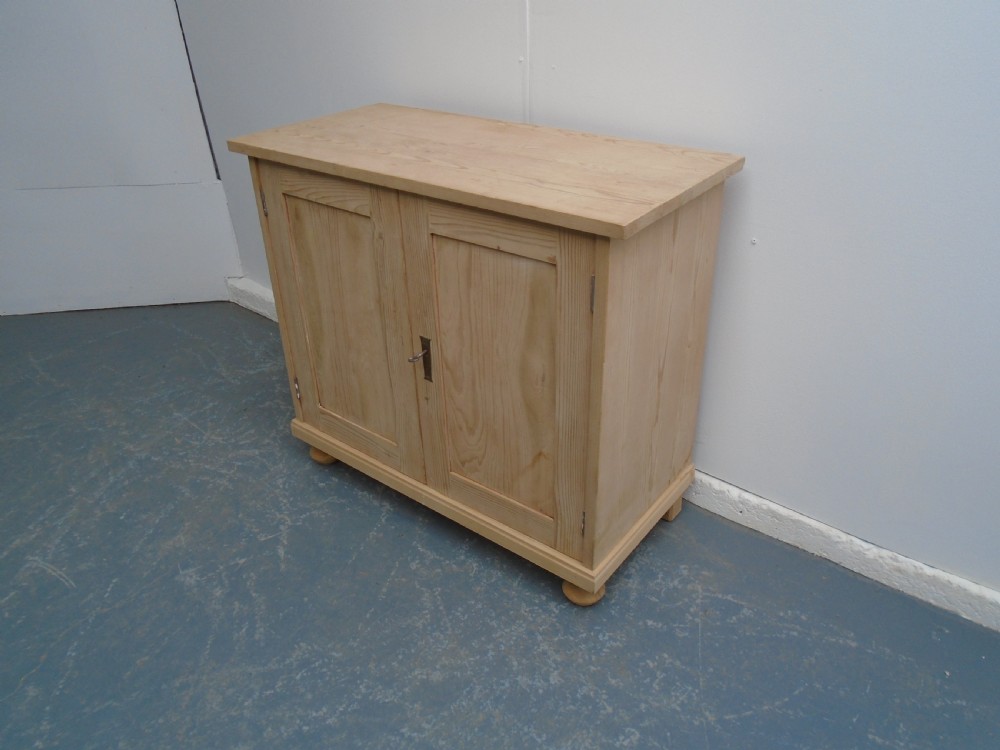 A low rectangular Victorian pine cupboard featuring two panelled doors, a central metal keyhole escutcheon, and turned bun feet.