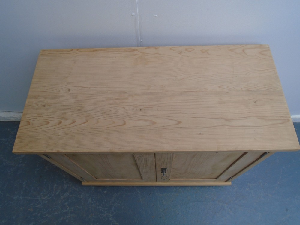 A low rectangular Victorian pine cupboard featuring two panelled doors, a central metal keyhole escutcheon, and turned bun feet. View VI