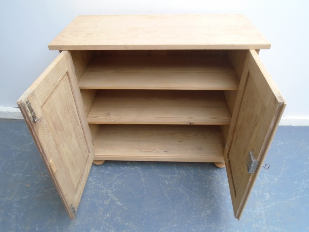 A low rectangular Victorian pine cupboard featuring two panelled doors, a central metal keyhole escutcheon, and turned bun feet. View VIII