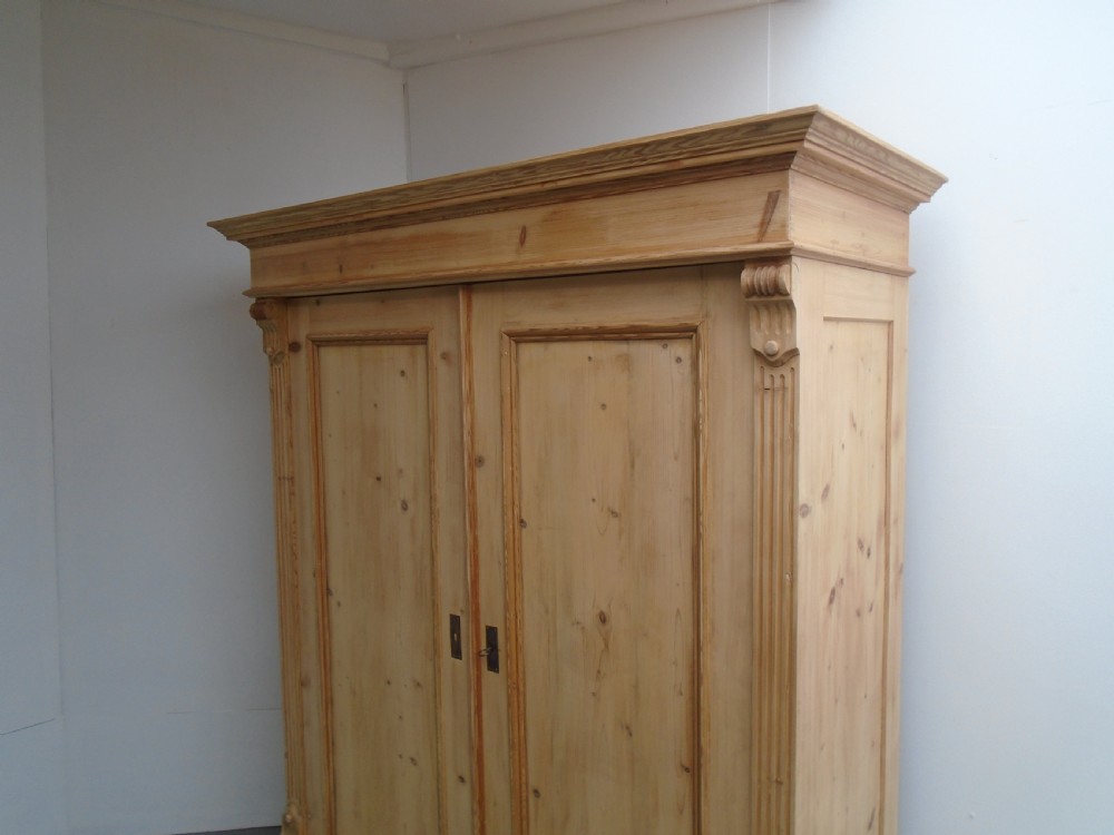 An unpainted Victorian pine double knockdown wardrobe featuring fluted side pilasters, panelled doors, a deep moulded cornice, and base drawers. View II