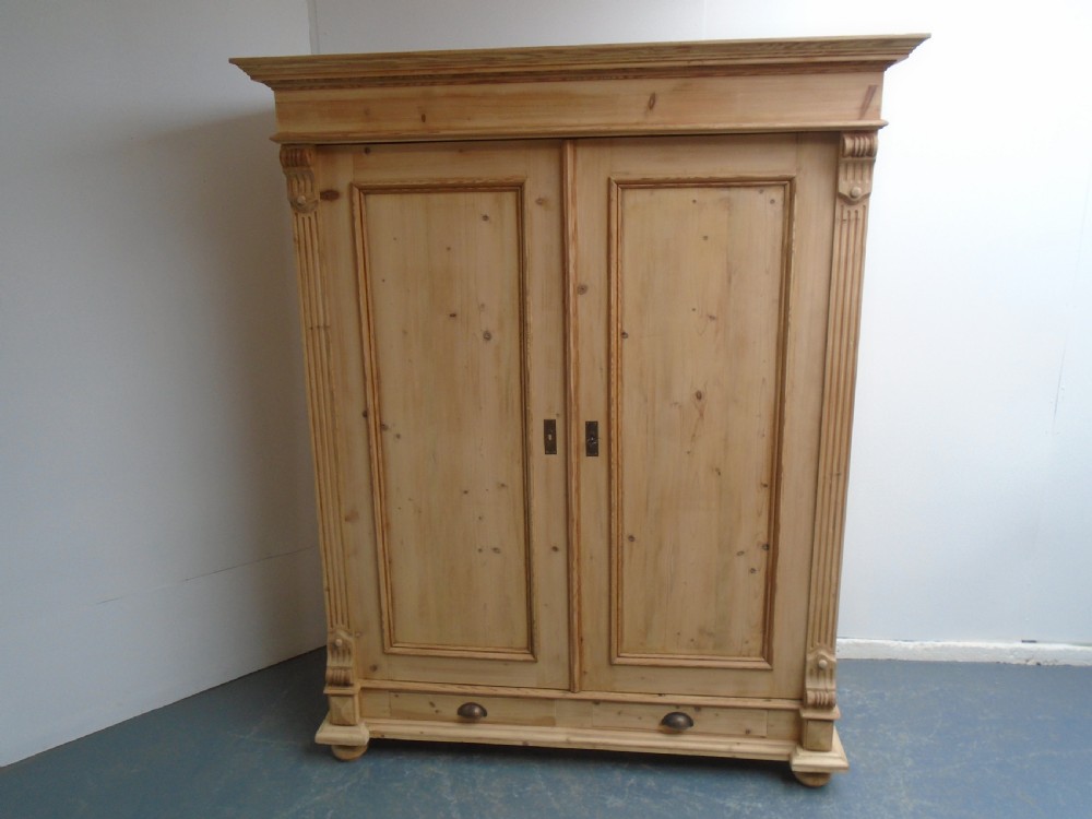 An unpainted Victorian pine double knockdown wardrobe featuring fluted side pilasters, panelled doors, a deep moulded cornice, and base drawers. View III