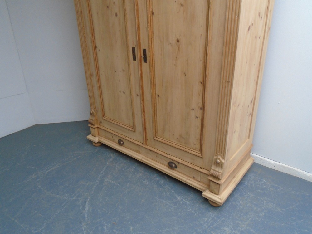 An unpainted Victorian pine double knockdown wardrobe featuring fluted side pilasters, panelled doors, a deep moulded cornice, and base drawers. View VI