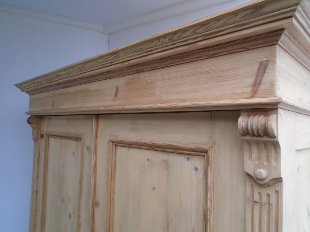 An unpainted Victorian pine double knockdown wardrobe featuring fluted side pilasters, panelled doors, a deep moulded cornice, and base drawers. View VIII
