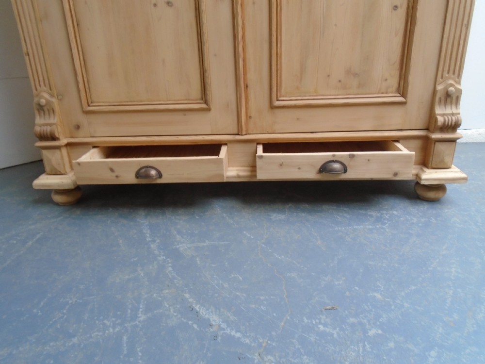 An unpainted Victorian pine double knockdown wardrobe featuring fluted side pilasters, panelled doors, a deep moulded cornice, and base drawers. View X