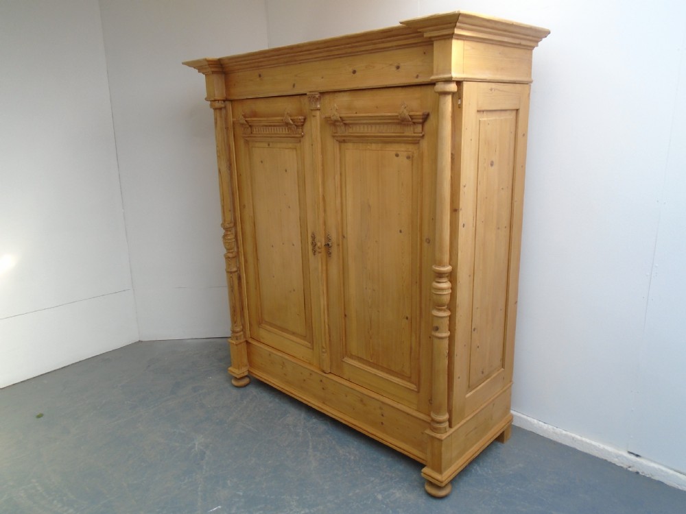 A large Victorian waxed pine double-door wardrobe featuring turned side columns, decorative pediments above the panelled doors, and a molded cornice.