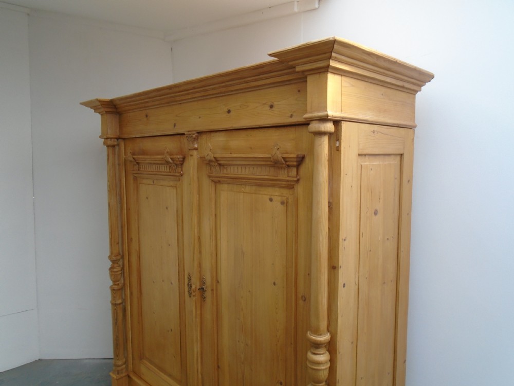 A large Victorian waxed pine double-door wardrobe featuring turned side columns, decorative pediments above the panelled doors, and a molded cornice. View II