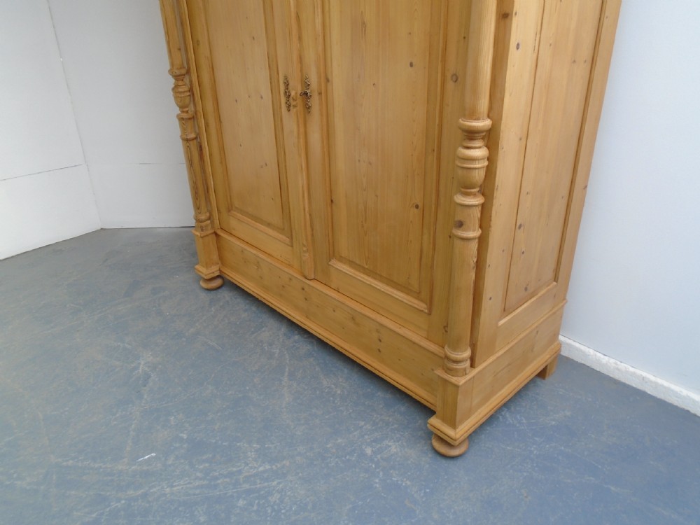 A large Victorian waxed pine double-door wardrobe featuring turned side columns, decorative pediments above the panelled doors, and a molded cornice. View III