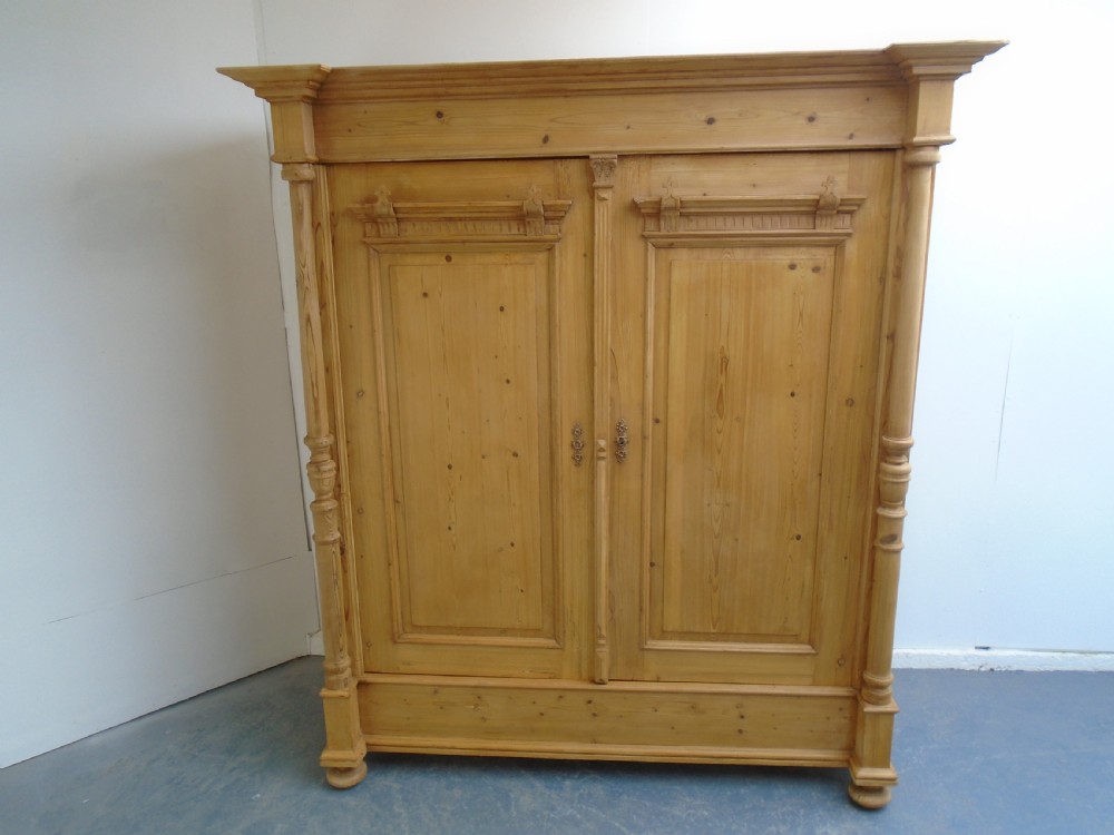 A large Victorian waxed pine double-door wardrobe featuring turned side columns, decorative pediments above the panelled doors, and a molded cornice. View V