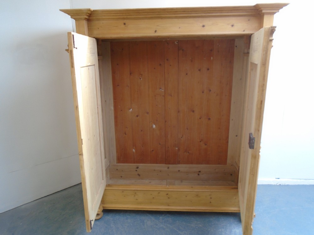 A large Victorian waxed pine double-door wardrobe featuring turned side columns, decorative pediments above the panelled doors, and a molded cornice. View X