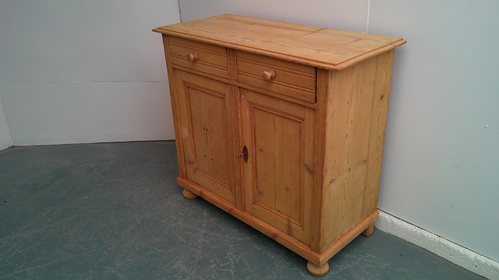 A Victorian pine dresser base featuring two drawers above a two-door cupboard with turned wooden knobs and bun feet.