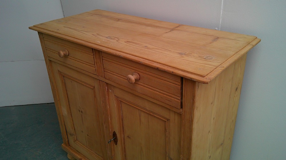 A Victorian pine dresser base featuring two drawers above a two-door cupboard with turned wooden knobs and bun feet. View II