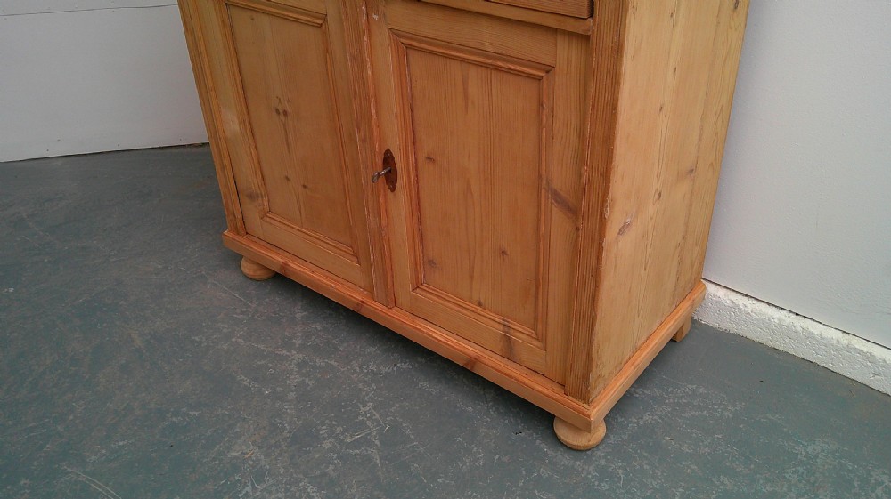 A Victorian pine dresser base featuring two drawers above a two-door cupboard with turned wooden knobs and bun feet. View III