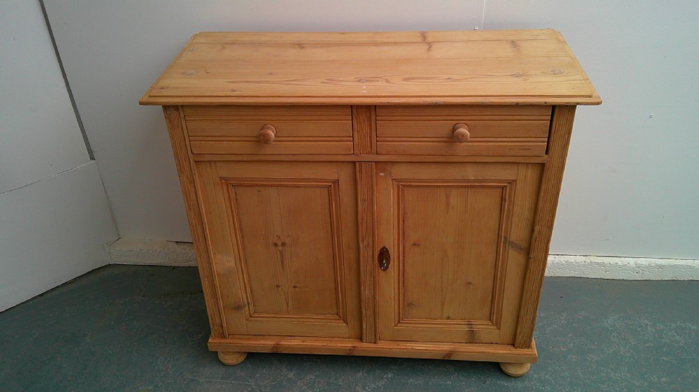 A Victorian pine dresser base featuring two drawers above a two-door cupboard with turned wooden knobs and bun feet. View IV