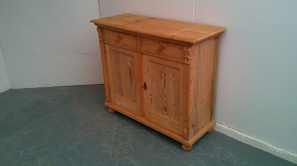 An early Victorian stripped pine shallow dresser base featuring two top drawers over a two-door panelled cupboard with turned bun feet.