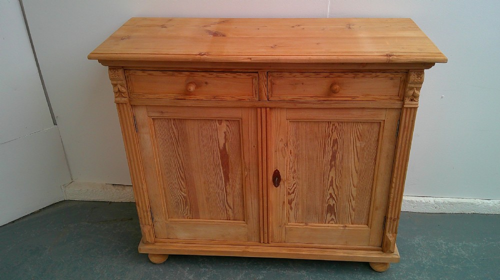 An early Victorian stripped pine shallow dresser base featuring two top drawers over a two-door panelled cupboard with turned bun feet. View II