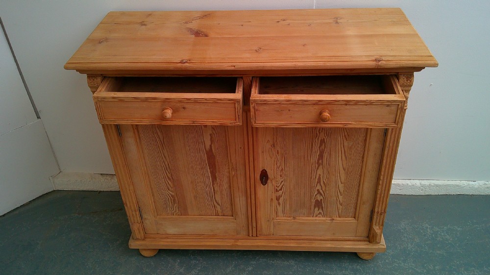 An early Victorian stripped pine shallow dresser base featuring two top drawers over a two-door panelled cupboard with turned bun feet. View X