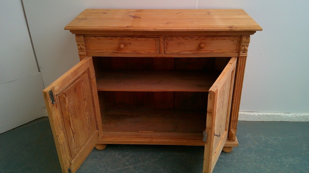 An early Victorian stripped pine shallow dresser base featuring two top drawers over a two-door panelled cupboard with turned bun feet. View XI