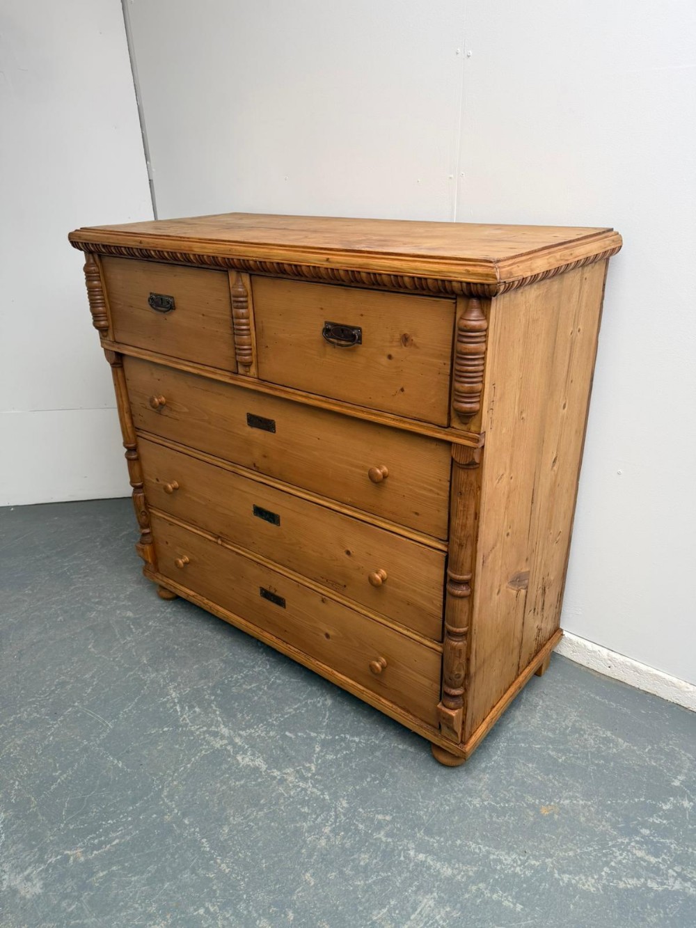 A large antique waxed pine chest of drawers featuring two small upper drawers over three full-width drawers with turned side columns.